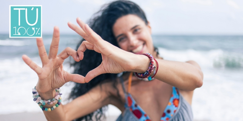 Mujer haciendo un corazon con las manos en la playa